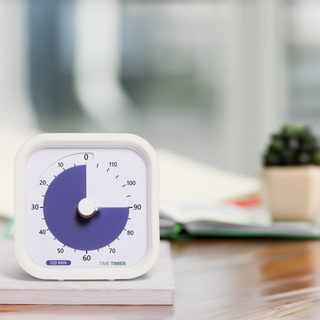 The Time Timer MOD - 120 Minute visual timer is shown on a tabletop, sitting on a book. The purple disk is set to 90 minutes. 