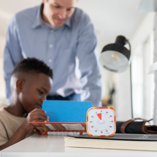 Little boy is reading his book with a male figure standing over him , smiling. A Time Timer is at the front showing how much reading time is left. 